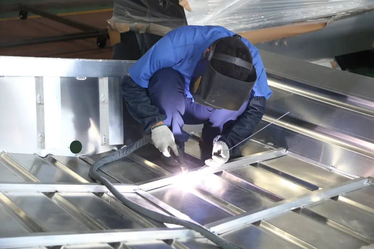 Worker welding metal framing inside a boat hull at the source factory